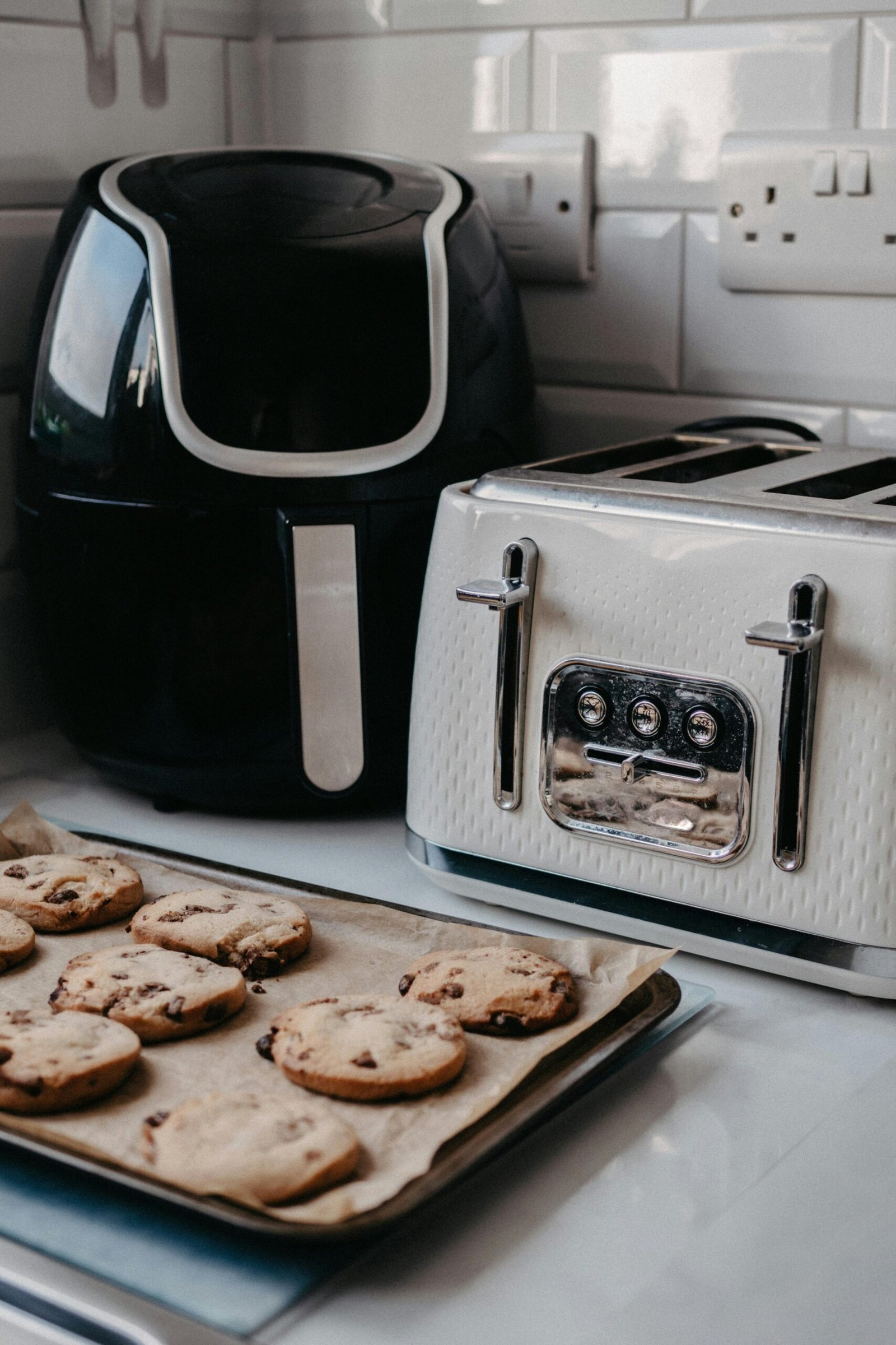 Freshly baked cookies on tray beside air fryer and toaster.